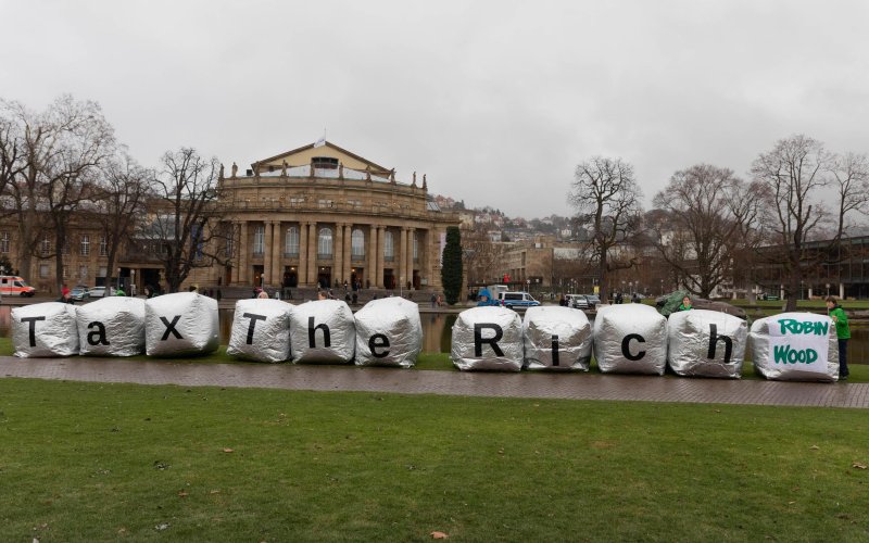 Aktivist*innen mit großen silbernen Würfeln vor der Stuttgarter Oper, Aufschrift: Tax The Rich