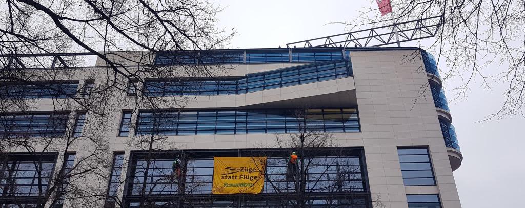 Zwei Kletter*innen haben sich mit einem Banner vor der Fassade des Willy-Brandt-Hauses in Berlin abgeseilt. Banner-Aufschrift: Flüge statt Züge! ROBIN WOOD