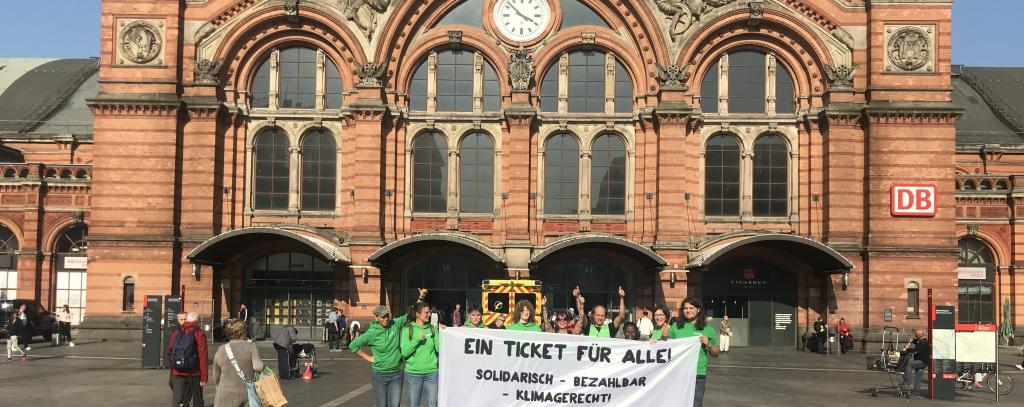 Gruppe mit Banner mit Aufschrift "Ein Ticket für alle" vor Bremer Hauptbahnhof