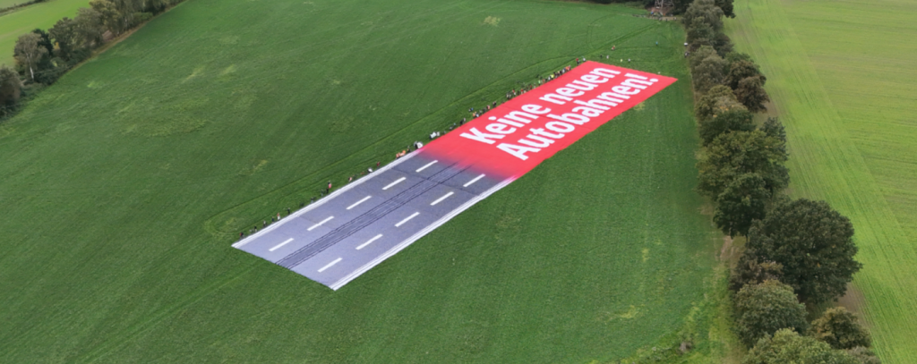 Drohnenfoto von Riesenransparent auf Wiese mit Autobahn
