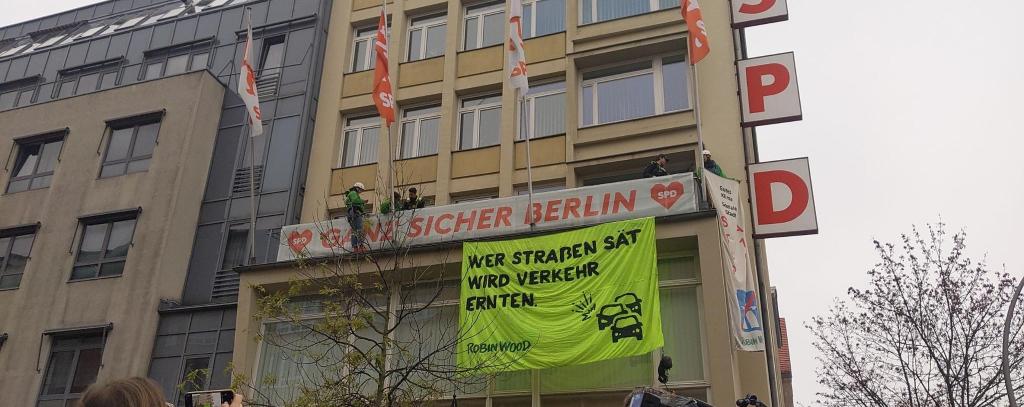 Kletter-Aktivist*innen haben ein Banner am Kurt-Schumacher-Haus der SPD in Berlin befestigt. Aufschrift: "Wer Straßen sät, wird Verkehr ernten. ROBIN WOOD"